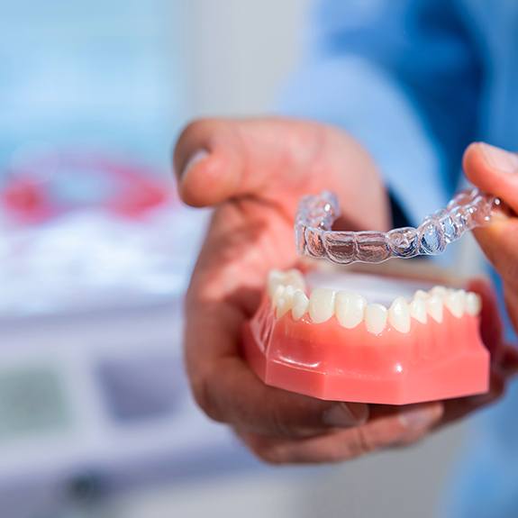 Dentist placing clear aligner on model of teeth