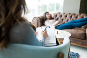 Therapist taking notes while young woman reclines on a couch in the background